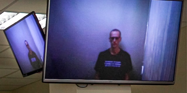 In this photo provided by the Babuskinsky District Court on Thursday, April 29, 2021, Russian opposition leader Alexei Navalny appears on TV screens via a video link from prison, during a hearing on his charges for defamation, in the Babuskinsky District Court in Moscow, Russia. The politician was convicted in February and ordered to pay a fine of 850-thousand rubles (the equivalent of $11,500). It was Navalny's first public appearance since his transfer to a penal colony last month. (Babuskinsky District Court Press Service via AP)