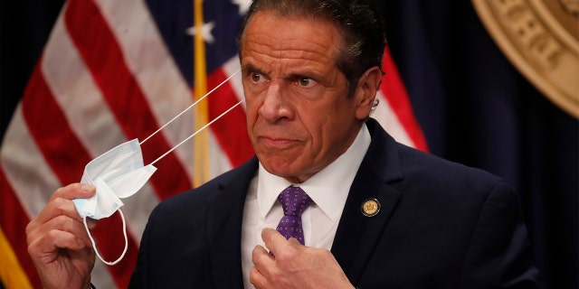 Gov. Andrew Cuomo takes off his face mask before a news conference in New York on Monday, April 19, 2021. (Shannon Stapleton/Pool via AP)