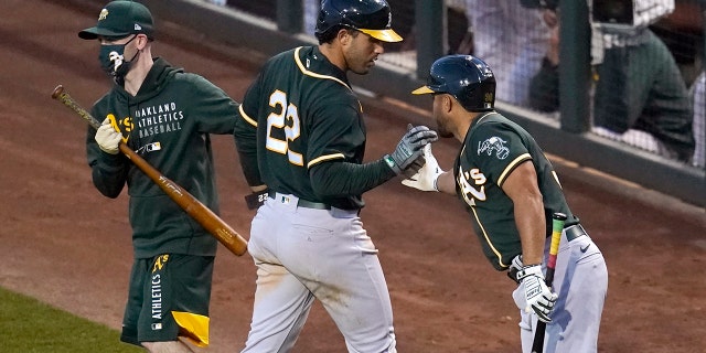 Oakland Athletics' Ramon Laureano (22) celebrates with Vimael Machin, right, and the bat boy while returning to the dugout after scoring against the Los Angeles Dodgers during the third inning of a spring training baseball game Friday, March 26, 2021, in Phoenix. (AP Photo/Ross D. Franklin)