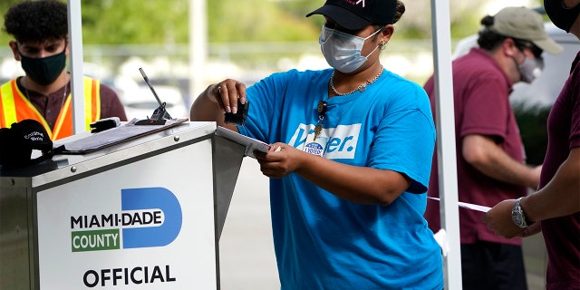 An election worker stamps a vote-by-mail ballot dropped off by a voter before placing it in an official ballot drop box before at the Miami-Dade County Board of Elections in Doral, Fla.