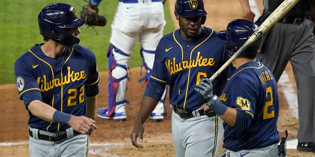 Milwaukee Brewers' Christian Yelich (22), Lorenzo Cain (6) and Luis Urias (2) celebrate after Yelich and Cain scored on an Orlando Arcia double in the sixth inning of a preseason baseball game against the Texas Rangers in Arlington, Texas, Monday, March 29, 2021. (AP Photo/Tony Gutierrez)