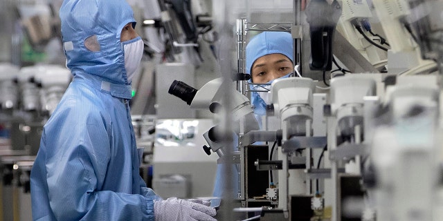 In this May 14, 2020 photo, employees wearing protective equipment work at a semiconductor production facility for Renesas Electronics during a government organized tour for journalists in Beijing.