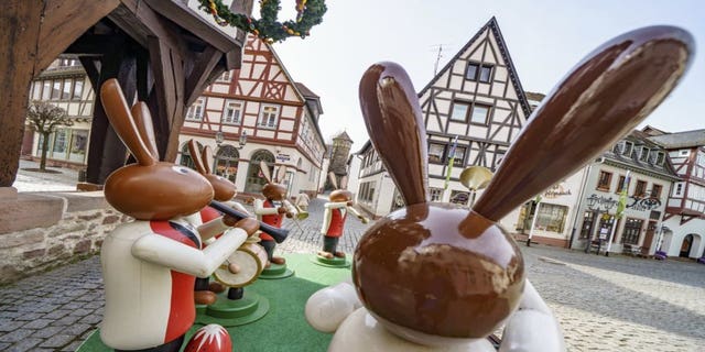 Human-sized wooden figures representing Easter bunnies playing music stand in front of Michelstadt's historic town hall, as they do every year, to spread Easter atmosphere in Michelstadt, Germany, Thursday, April 1, 2021. However, the popular meeting place in the heart of the town in the Odenwald was almost deserted on Thursday morning due to the pandemic. (Frank Rumpenhorst/dpa via AP)
