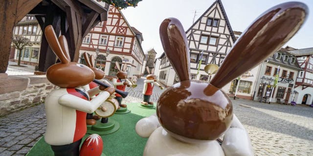 Human-sized wooden figures representing Easter bunnies playing music stand in front of Michelstadt's historic town hall, as they do every year, to spread Easter atmosphere in Michelstadt, Germany, Thursday, April 1, 2021. However, the popular meeting place in the heart of the town in the Odenwald was almost deserted on Thursday morning due to the pandemic. (Frank Rumpenhorst/dpa via AP)