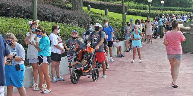 Guests in protective masks wait to pick up their tickets at the Magic Kingdom theme park at Walt Disney World on the Florida theme park's reopening day, July 11, 2020. (GREGG NEWTON/Gregg Newton/AFP via Getty Images)