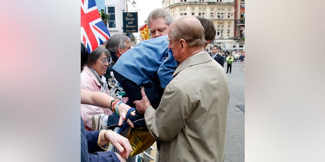 Prince Philip, Duke of Edinburgh lifts a young boy over the barriers as he and Queen Elizabeth II undertake a walkabout outside Windsor Castle to meet members of the public who have gathered on her 80th birthday on April 21, 2006, in Windsor, England.