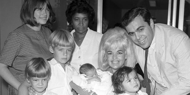 Actress Jayne Mansfield and family are pictured here as the blonde actress leaves Cedars of Lebanon Hospital with the newest addition to the family, baby Anthony. Left to right are Jayne Marie Mansfield, 15, Zoltan Hargitay, 5, Mickey Hargitay Jr., 6, unidentified hospital attendant, Jayne holding baby Anthony, and husband Matt Cimber with Mariska Hargitay, 1. Anthony is the first child by Cimber.