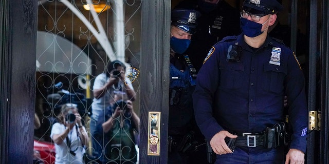 Members of the media are reflected in the widow a door as New York City Police officers walk out of the apartment building where former New York Mayor Rudy Giuliani resides, Wednesday, April 28, 2021, in New York.