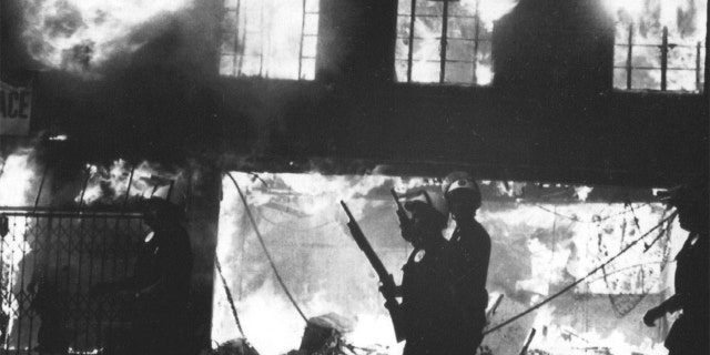GLI ANGELI, CALIFORNIA - APRILE 30: Police officers stand watch over burning building in West Los Angeles following looting and arson reaction to the acquittal of four LAPD officers in the Rodney King incident. Photographed April 30, 1992 a Los Angeles, QUELLO. (Photo by Fred Sweets/The Washington Post via Getty Images)