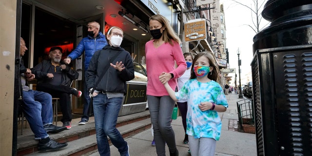 People walking down the street are shown wearing masks against COVID-19.