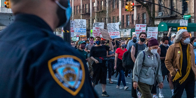 Police officers keep a watchful eye as peaceful protesters march down Flatbush Avenue on Tuesday, April 20, 2021, in the Brooklyn borough of New York.