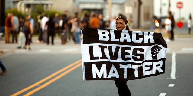 A protester carries a Black Lives Matter flag shortly before the start of a dawn to dusk curfew following the killing of Andrew Brown Jr. by sheriffs last week, in Elizabeth City, North Carolina, U.S. April 27, 2021. REUTERS/Jonathan Drake