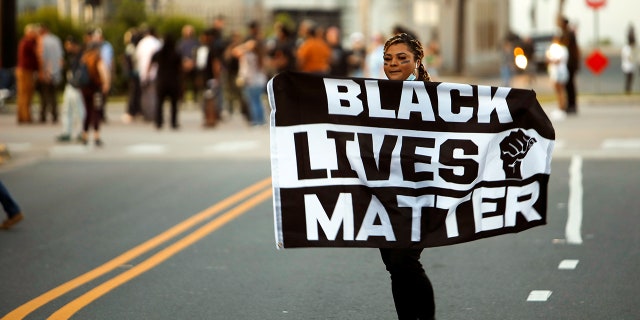 A protester carries a Black Lives Matter flag shortly before the start of a dawn to dusk curfew following the killing of Andrew Brown Jr. by sheriffs last week, in Elizabeth City, North Carolina, U.S. April 27, 2021. REUTERS/Jonathan Drake