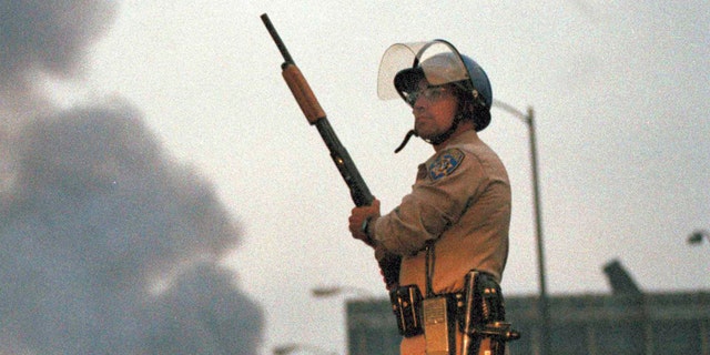 A California Highway Patrol officer stands guard at Ninth Street and Vermont Avenue in Los Angeles as smoke rises from a fire further down the street, April 30, 1992. It was the second day of unrest in Los Angeles following the acquittal of four Los Angeles police officers in the Rodney King beating case. (AP Photo/David Longstreath)