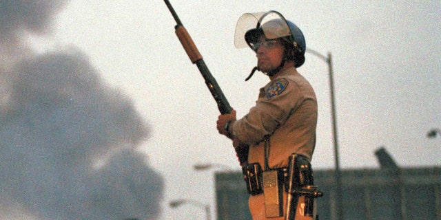 A California Highway Patrol officer stands guard at Ninth Street and Vermont Avenue in Los Angeles as smoke rises from a fire further down the street, April 30, 1992. It was the second day of unrest in Los Angeles following the acquittal of four Los Angeles police officers in the Rodney King beating case. (AP Photo/David Longstreath)