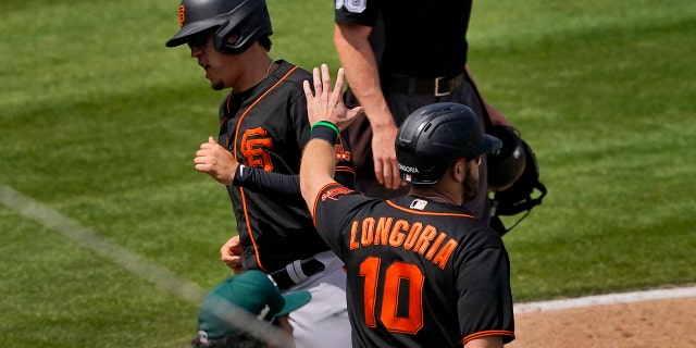 San Francisco Giants' Wilmer Flores and Evan Longoria (10) score on a double hit by Curt Casali during the third inning of a spring training baseball game against the Oakland Athletics, Monday, March 29, 2021, in Mesa, Ariz. (AP Photo/Matt York)