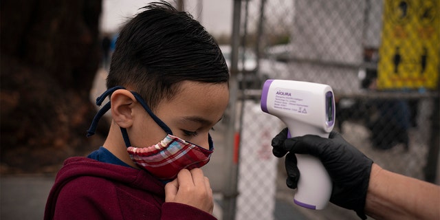 Adam Alvarado, 6, gets his temperature checked on the first day of in-person learning at Heliotrope Avenue Elementary School in Maywood, Calif., Tuesday, April 13, 2021. (AP Photo/Jae C. Hong)