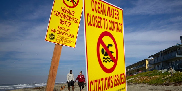 A couple walks along the beach as signs warn of contaminated water at Imperial Beach, Calif on Dec. 12, 2018. (AP Photo/Gregory Bull, File)