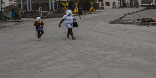 A woman and a girl walk wearing protective head coverings walk on a street covered with volcanic ash a day after the La Soufriere volcano erupted, in Kingstown, on the eastern Caribbean island of St. Vincent, Saturday, April 10, 2021. (AP Photo/Lucanus Ollivierre)