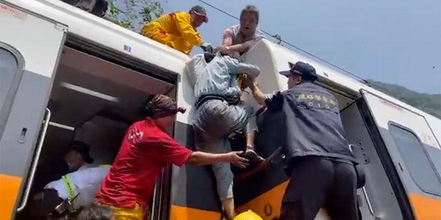 A passenger, center, is helped to climb out of the derailed train. (AP/hsnews.com.tw)