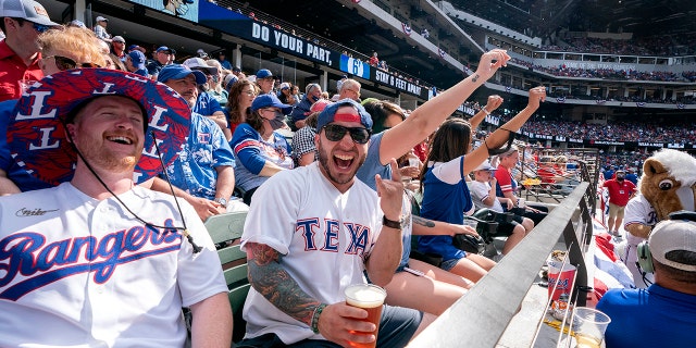 Texas Rangers fans Cameron Leverett, links, and Anthony Sosa celebrate during the fourth inning of a baseball game against the Toronto Blue Jays Monday, April 5, 2021, in Arlington, Texas. (AP Photo/Jeffrey McWhorter)