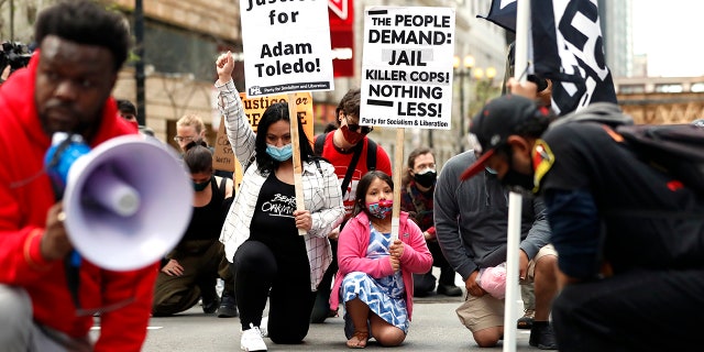 Abigail Garcia, 7, right, takes a knee with her mother Judith Garcia and other protestors during a peaceful protest on Tuesday, April 13, 2021, in downtown Chicago, demanding justice for Daunte Wright and Adam Toledo, who were shot dead by police. (AP Photo/Shafkat Anowar)