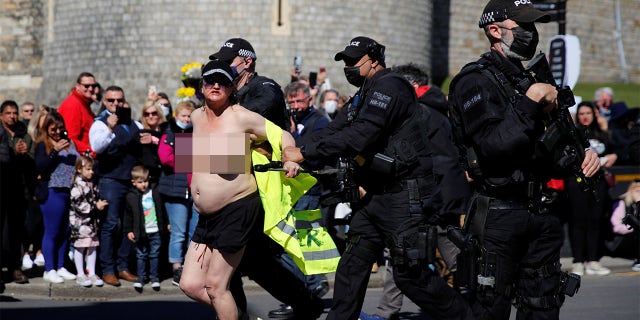 SENSITIVE MATERIAL. THIS IMAGE MAY OFFEND OR DISTURB. A protester runs outside Windsor Castle on the day of the funeral of Britain's Prince Philip, husband of Queen Elizabeth, who died at the age of 99, in Windsor, Britain, April 17, 2021.