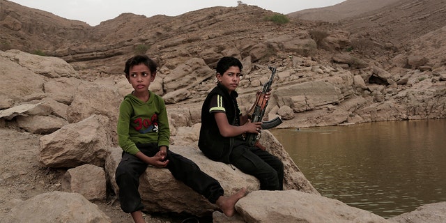 在这张2018年7月30日的档案照片中，一名17岁的男孩在也门马里布的大坝上拿着武器。