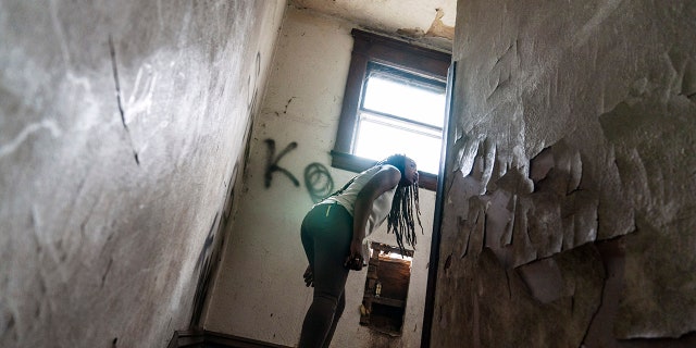 游行 18, 2021: Cox peers around a stairwell while walking through an abandoned home frequented by people struggling with addiction, 在亨廷顿, 瓦.
