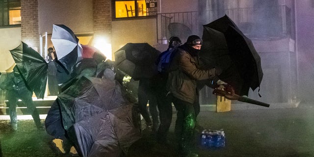 Demonstrators protect themselves with umbrellas and a blower against tear gas and pepper balls outside the Brooklyn Center police station on Tuesday. (Photo by KEREM YUCEL/AFP via Getty Images)