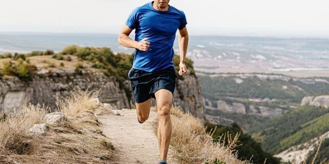 Male runner running mountain trail on edge of cliff.