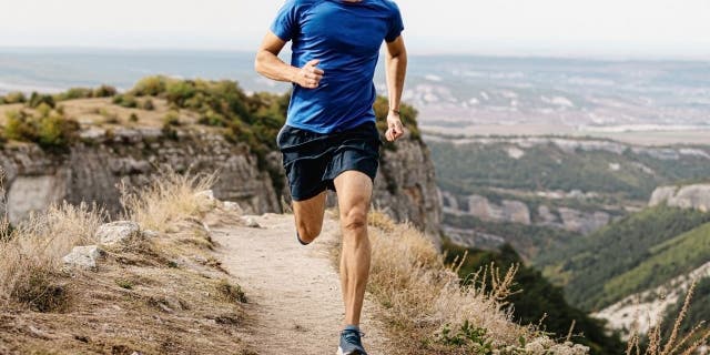 Male runner running mountain trail on edge of cliff.