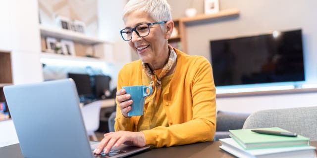 Senior woman working at home using laptop computer in the living room