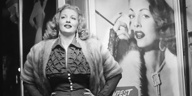 American stripper Tempest Storm poses next to a promotional poster for her burlesque act in front of a theater, 1954. (Getty Images)