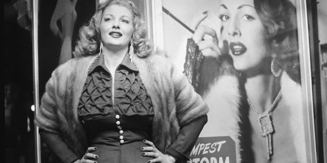 American stripper Tempest Storm poses next to a promotional poster for her burlesque act in front of a theater, 1954. (Getty Images)