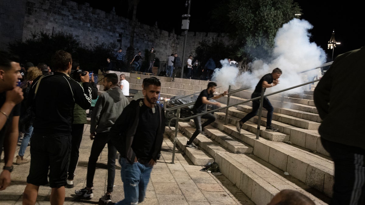 Palestinians react to stun grenades fired by Israeli police to clear the Damascus Gate to the Old City of Jerusalem after clashes at the Al-Aqsa Mosque compound, Friday, May 7, 2021. Palestinian worshippers clashed with Israeli police late Friday at the holy site sacred to Muslims and Jews, in an escalation of weeks of violence in Jerusalem that has reverberated across the region. (AP Photo/Maya Alleruzzo)