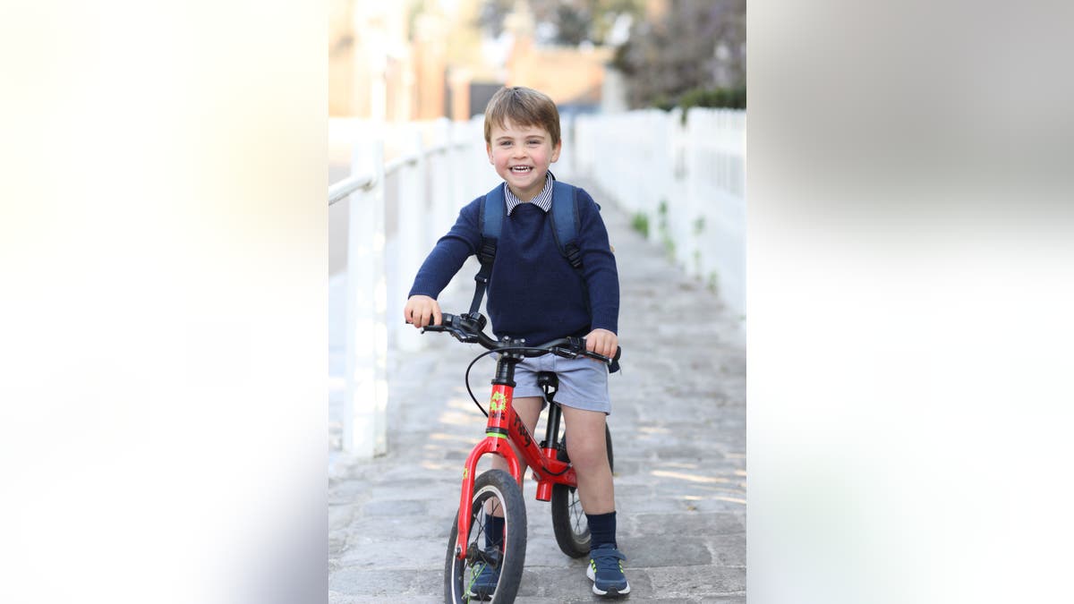 Prince Louis riding his red bike in a blue sweater