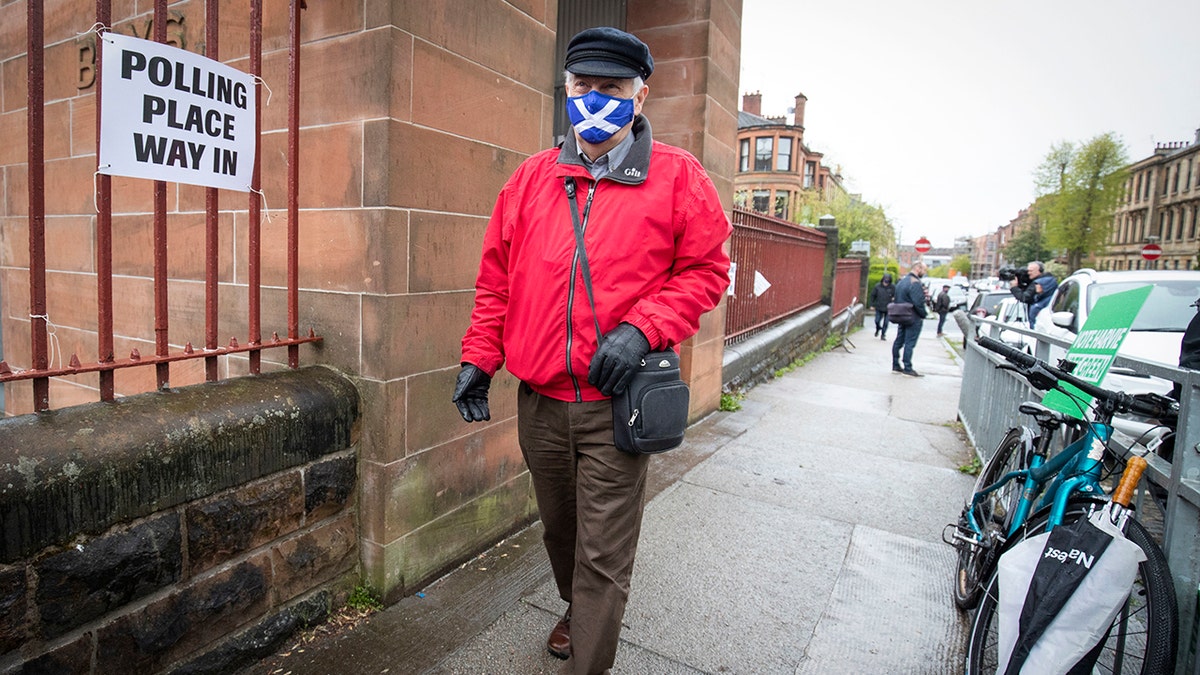 A man wearing a face mask arrives to vote at a polling station in Glasgow, Scotland, Thursday May 6, 2021.