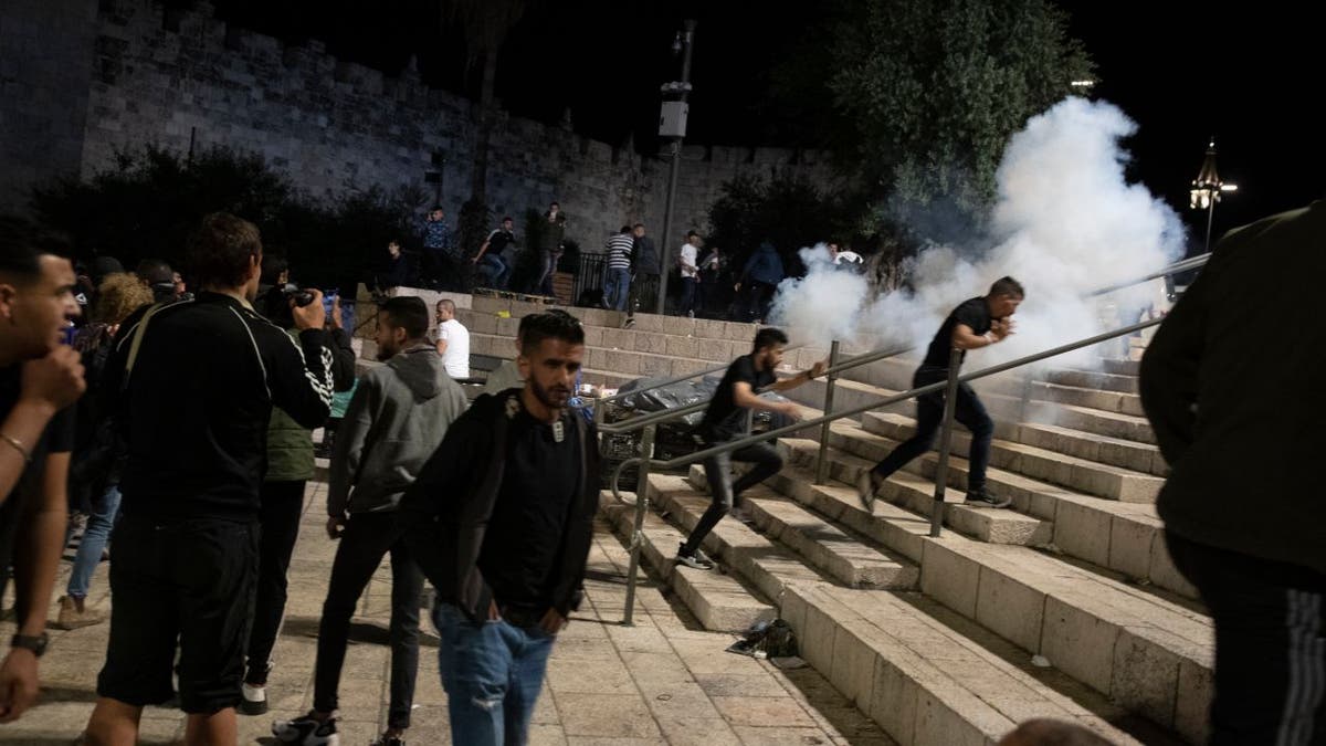 Palestinians react to stun grenades fired by Israeli police to clear the Damascus Gate to the Old City of Jerusalem after clashes at the Al-Aqsa Mosque compound, Friday, May 7, 2021. Palestinian worshippers clashed with Israeli police late Friday at the holy site sacred to Muslims and Jews.