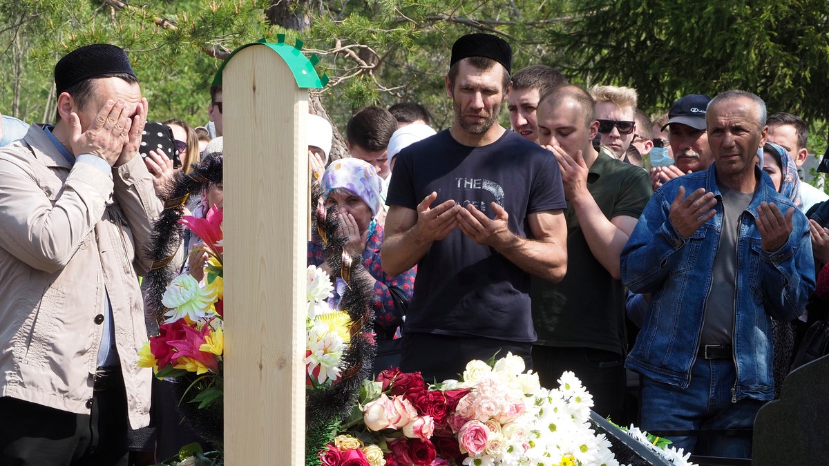 People pray next to the grave of Elvira Ignatieva, an English language teacher who was killed at a school shooting on Tuesday in Kazan, Russia, Wednesday, May 12, 2021. Russian officials say a gunman attacked a school in the city of Kazan and Russian officials say several people have been killed. Officials said the dead in Tuesday's shooting include students, a teacher and a school worker. Authorities also say over 20 others have been hospitalised with wounds. (AP Photo/Dmitri Lovetsky)