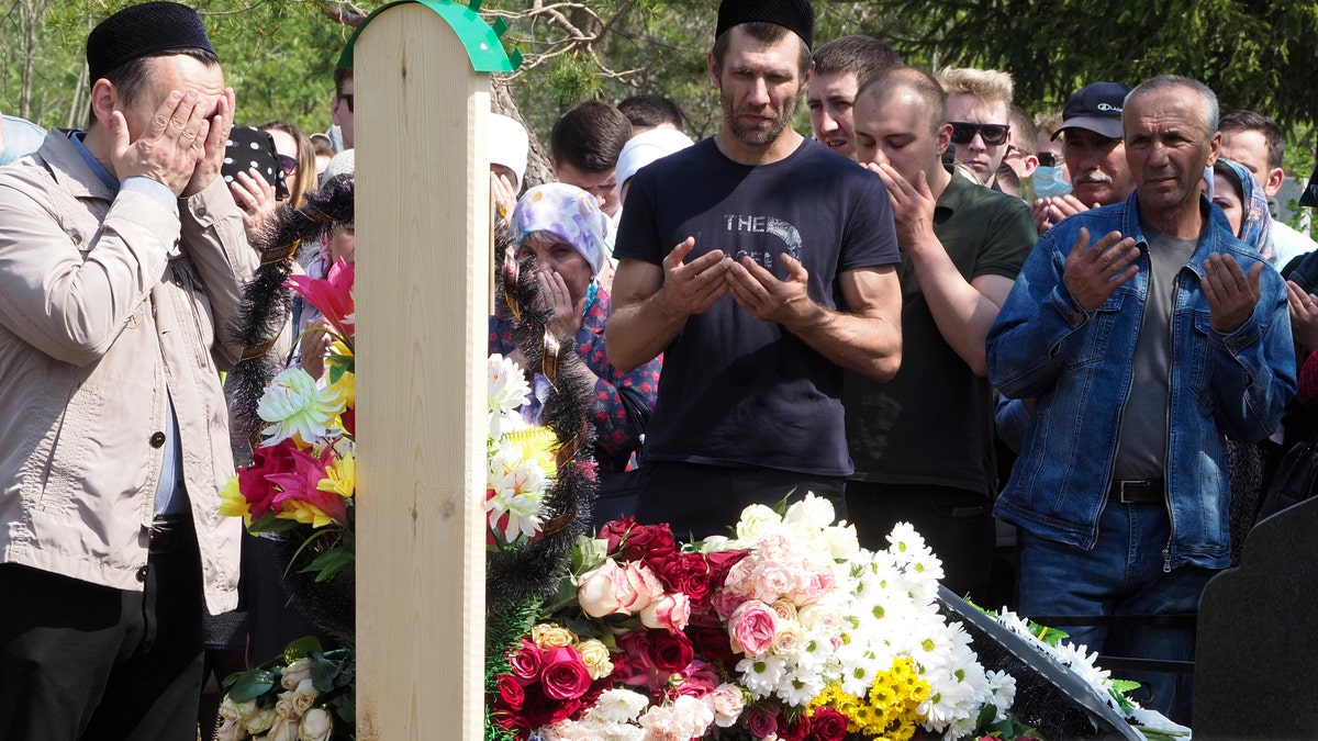 People pray next to the grave of Elvira Ignatieva, an English language teacher who was killed at a school shooting on Tuesday in Kazan, Russia, Wednesday, May 12, 2021. Russian officials say a gunman attacked a school in the city of Kazan and Russian officials say several people have been killed. Officials said the dead in Tuesday's shooting include students, a teacher and a school worker. Authorities also say over 20 others have been hospitalised with wounds. (AP Photo/Dmitri Lovetsky)