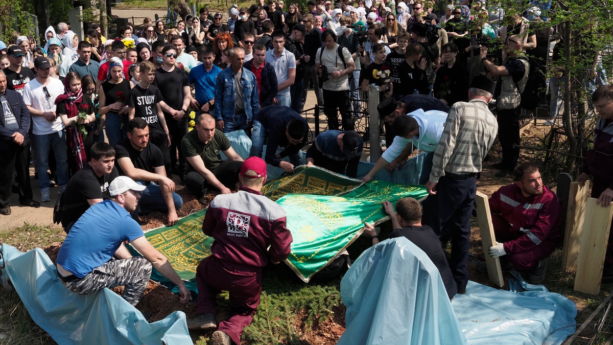People gather next to the grave during a funeral of Elvira Ignatieva, an English language teacher who was killed at a school shooting on Tuesday, in Kazan, Russia, Wednesday, May 12, 2021. Russian officials say a gunman attacked a school in the city of Kazan and Russian officials say several people have been killed. Officials said the dead in Tuesday's shooting include students, a teacher and a school worker. Authorities also say over 20 others have been hospitalised with wounds. (AP Photo/Dmitri Lovetsky)