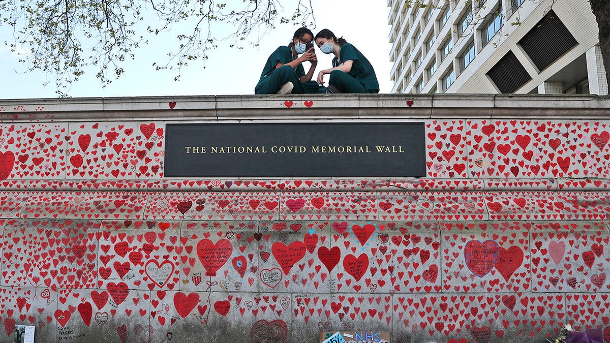 FILE - In this Tuesday, April 27, 2021 file photo, nurses from the nearby St Thomas' hospital sit atop the National Covid Memorial Wall in London.