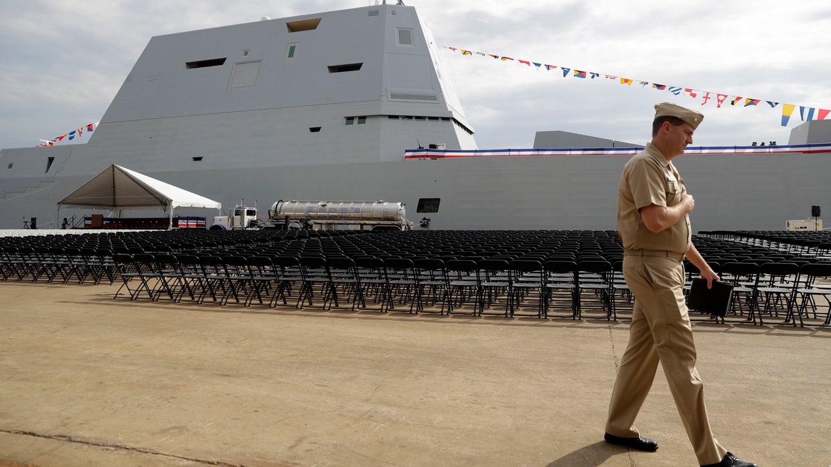 A member of the U.S. Navy walks past the future USS Zumwalt in Baltimore, in this Thursday, Oct. 13, 2016, file photo. The electric-drive, angular Zumwalt was commissioned into service, but its 155mm advanced gun system is being scrapped because its munitions are too expensive. (AP Photo/Patrick Semansky, File)