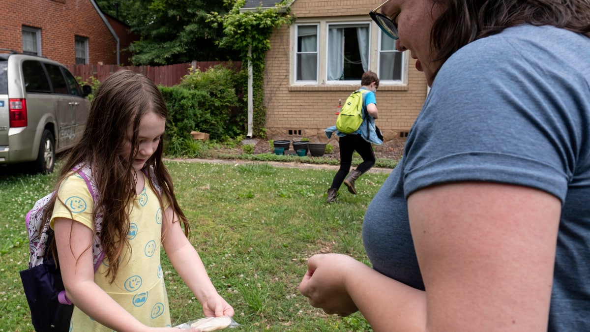 Abby Norman, right, looks at a project made by her daughter Priscilla, 9, left, as Juliet, 11, runs inside as they arrive home from school to the family's home in Decatur, Ga., Tuesday, May 18, 2021. Priscilla was in tears the first morning of school testing this year because she felt pressure to do well, but didn't feel prepared after remote learning. (AP Photo/Ben Gray)