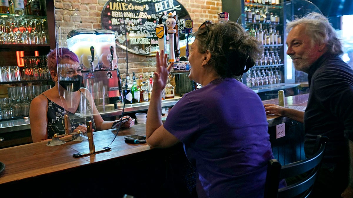 e's Bar co-owner Erin Ballard, left, talks to regulars Julie and Steve Ross at the bar on Manhattan's Upper West Side, Monday, May 17, 2021, in New York. The Ross's said they're "veterans, part of the family." "We discovered them during the pandemic in 24 degree-weather, while we were still wearing sweaters, mittens and long underwear. It's been a little oasis of sanity," said Steve Ross, right. "We feel the energy" of social life gearing back up," Bellard said. "People are so excited to be out." (AP Photo/Kathy Willens)