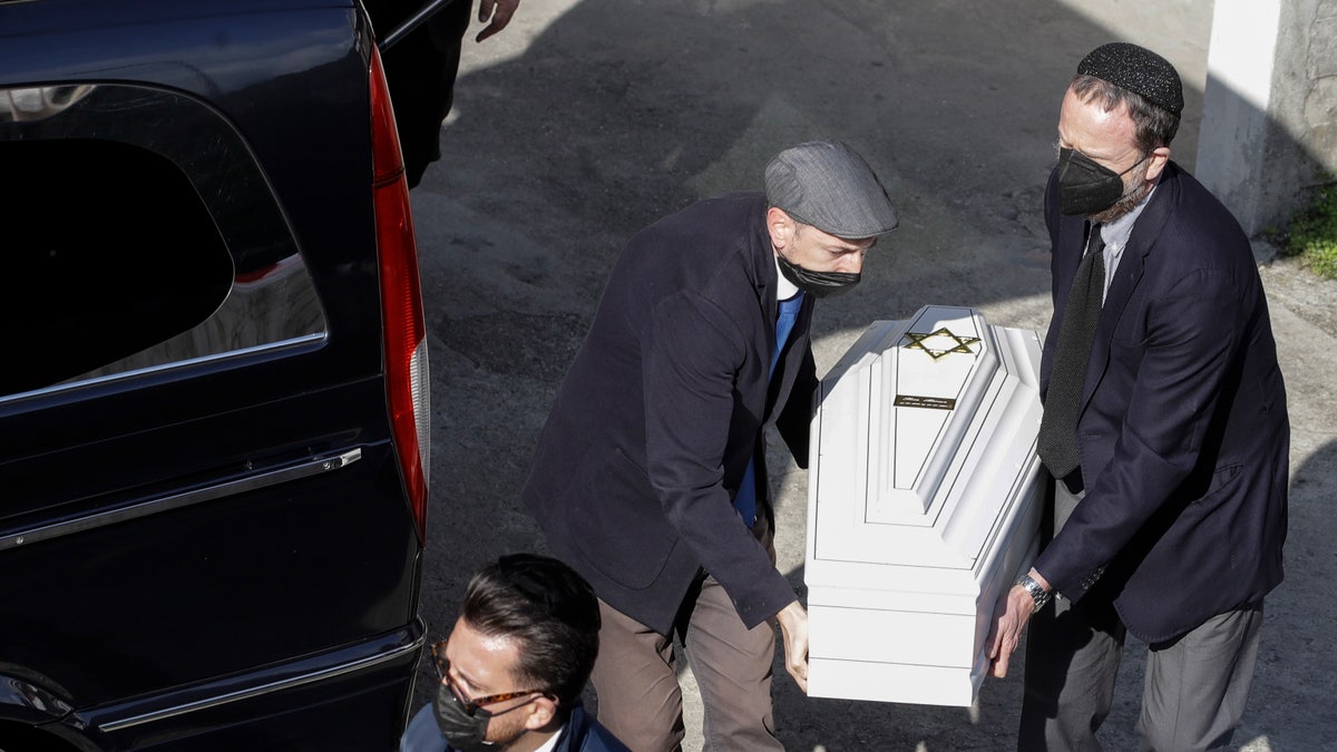 A white coffin is carried by members of the Jewish community at the morgue of Verbania Hospital, in Verbania, Italy, Wednesday, May 26, 2021. A prayer ceremony for the Jewish victims took place in Verbania Wednesday morning, before the bodies of the dead were released to return to their homes for funerals and burials. Three people were arrested following a cable car disaster that killed 14 people, after the lead cable apparently snapped and the cabin careened back down the mountain until it pulled off the line and crashed to the ground. (AP Photo/Luca Bruno)
