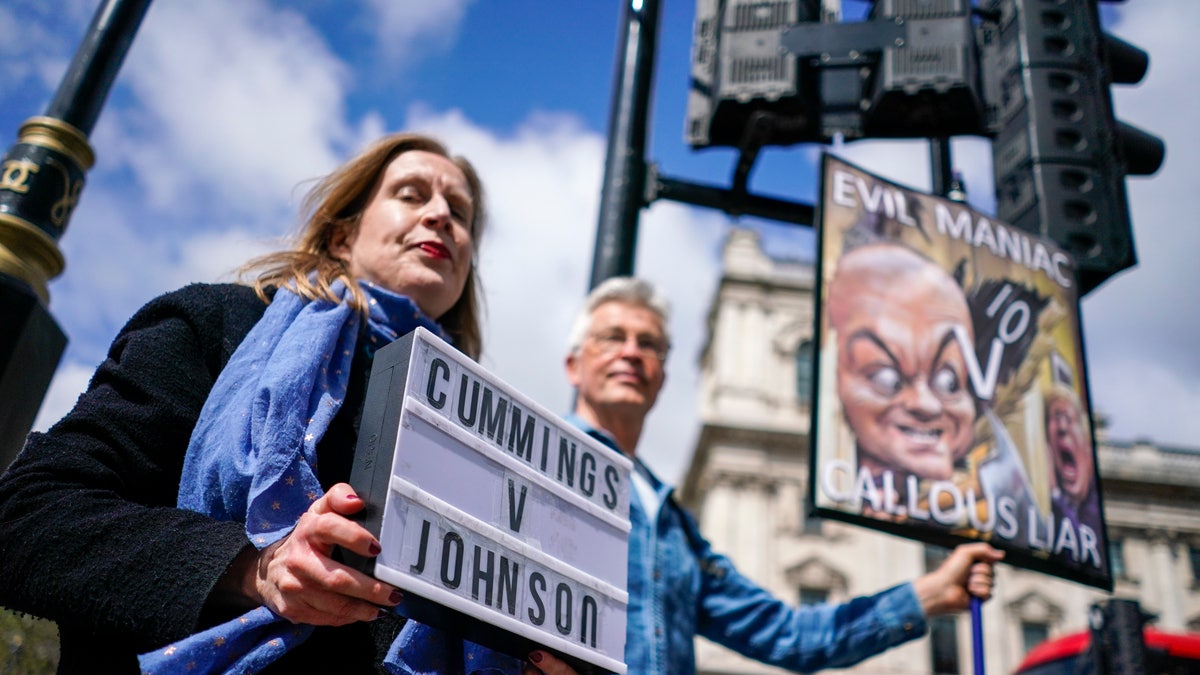 Protesters hold placards near Parliament Square, in London, on the day Dominic Cummings, the volatile advisor who until late last year was British Prime Minister Boris Johnson's most powerful and trusted aide, attended a select committee hearing at Portcullis House nearby, Wednesday, May 26, 2021. In recent days, Cummings has directed a torrent of criticism at Johnson's Conservative government in an ever-lengthening string of Twitter posts. On Wednesday, he plans to make the claims in person, testifying on live television to lawmakers investigating Britain's handling of COVID-19. (AP Photo/Alberto Pezzali)