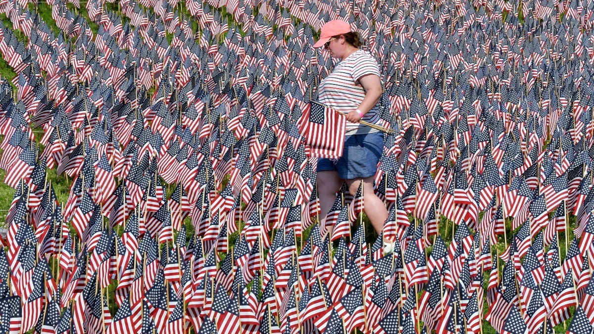 A volunteer walks through a field of American flags planted on Boston Common Wednesday, May 26, 2021, in Boston. (AP Photo/Josh Reynolds)