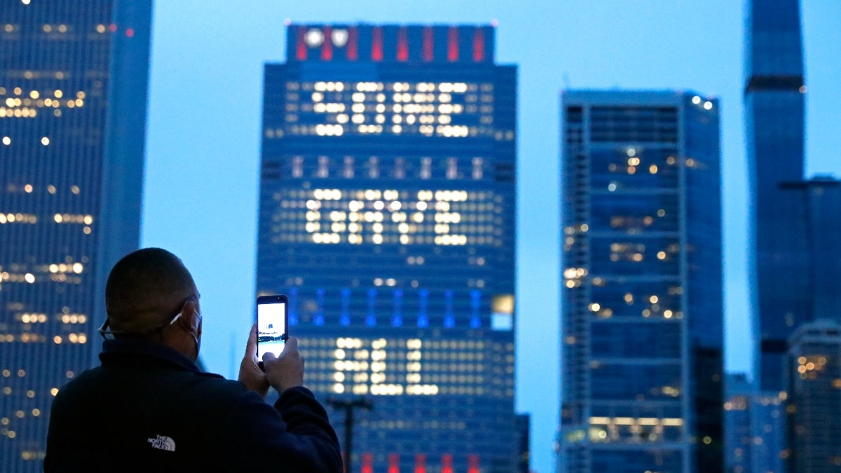 A person takes a photo, Sunday, May 30, 2021, of an illuminated sign on Chicago's Blue Cross Blue Shield Tower displaying "Some Gave All" in honor of Memorial Day. (AP Photo/Shafkat Anowar)